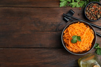 Photo of Delicious Korean carrot salad, oil, spices and parsley on wooden table, flat lay. Space for text