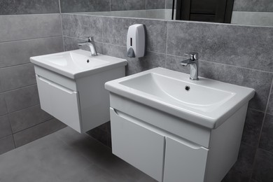 Photo of Public toilet interior with stylish white sinks and grey tiles
