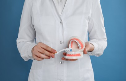 Photo of Dentist with jaws model and toothbrush on light blue background, closeup. Oral care demonstration
