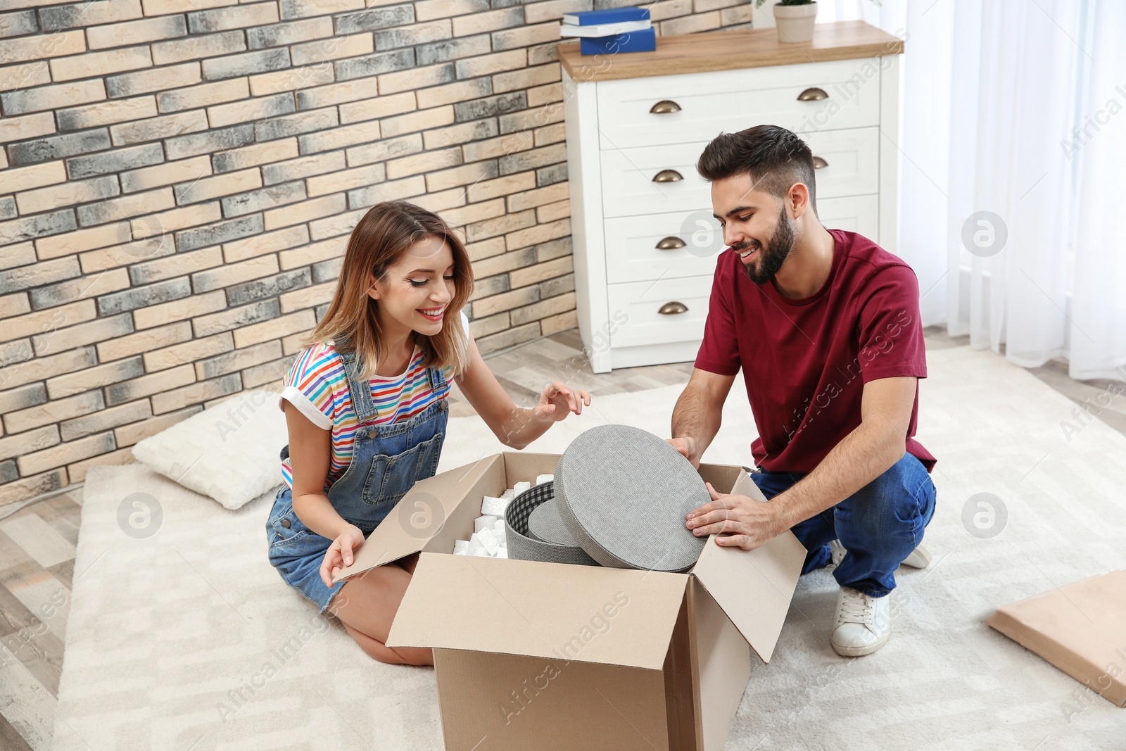 Photo of Young couple opening parcel on floor at home