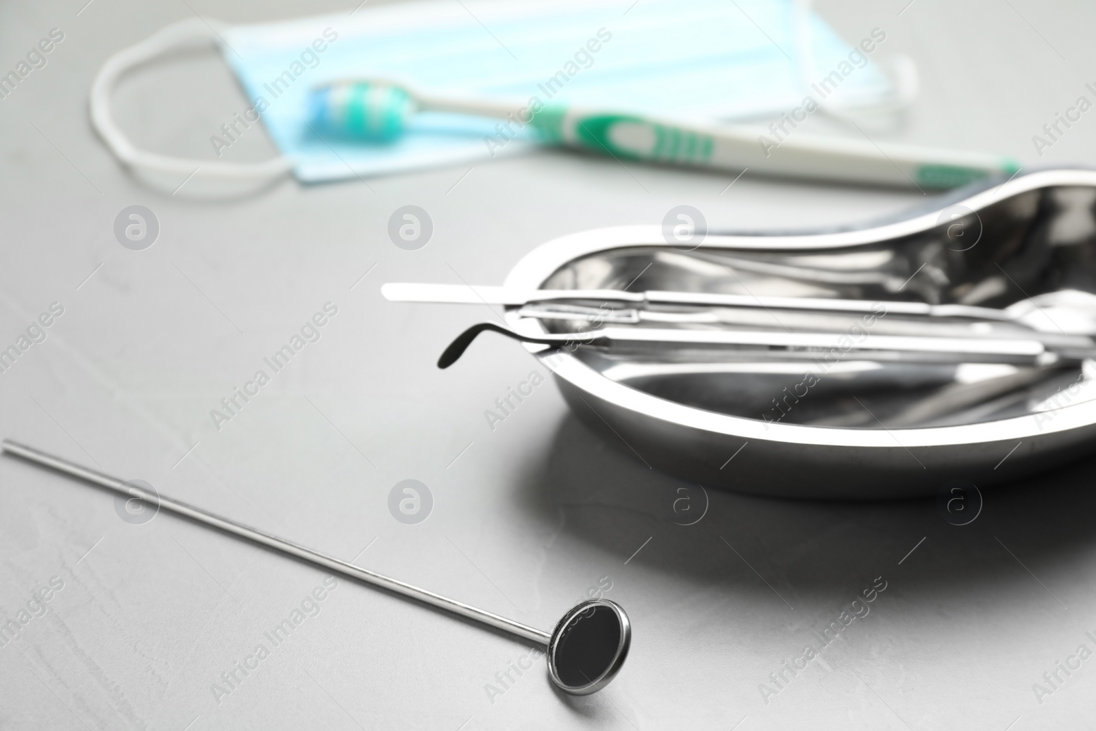 Photo of Mouth mirror near kidney shaped tray with dentist's tools on grey table, closeup