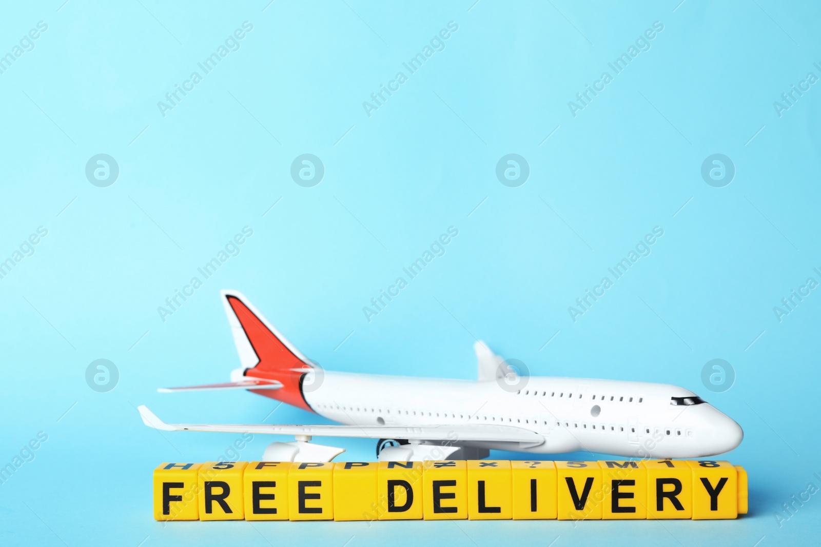 Photo of Toy plane and cubes with words FREE DELIVERY on light blue background, space for text. Logistics and wholesale concept