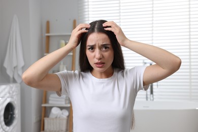 Photo of Emotional woman examining her hair and scalp in bathroom. Dandruff problem