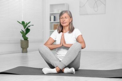 Senior woman practicing yoga on mat at home