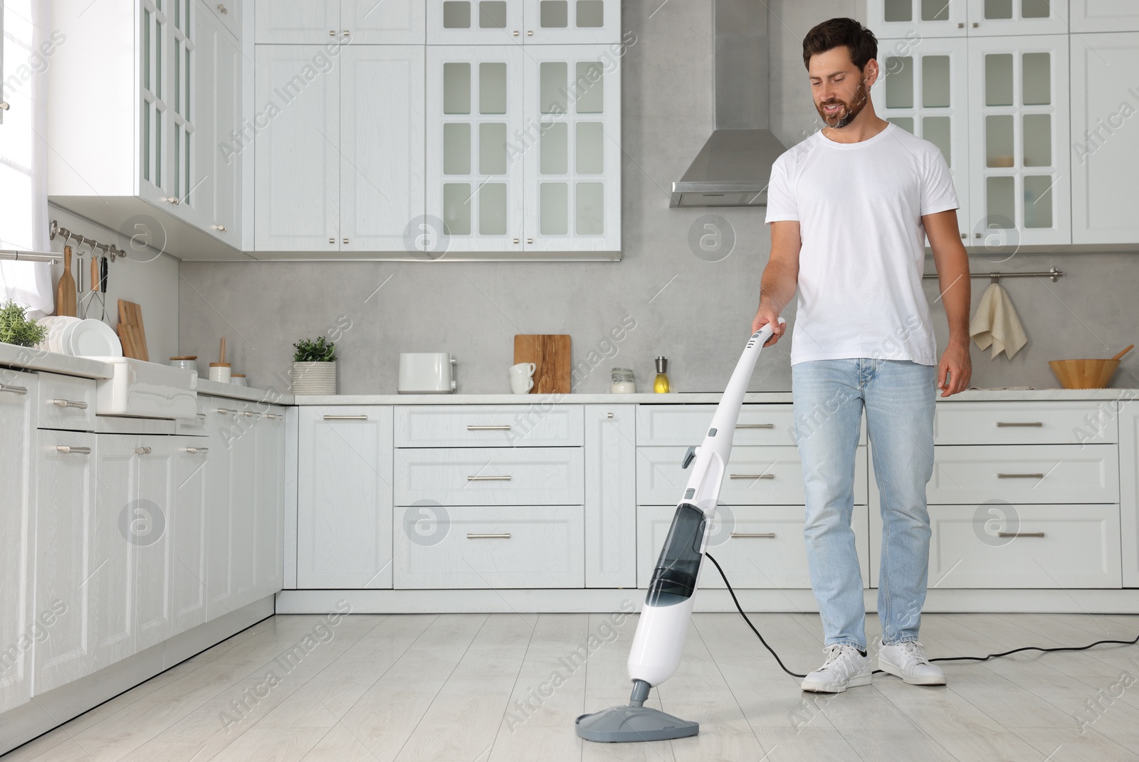 Photo of Happy man cleaning floor with steam mop in kitchen at home. Space for text