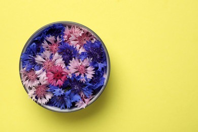 Beautiful colorful cornflowers in bowl on yellow background, top view. Space for text
