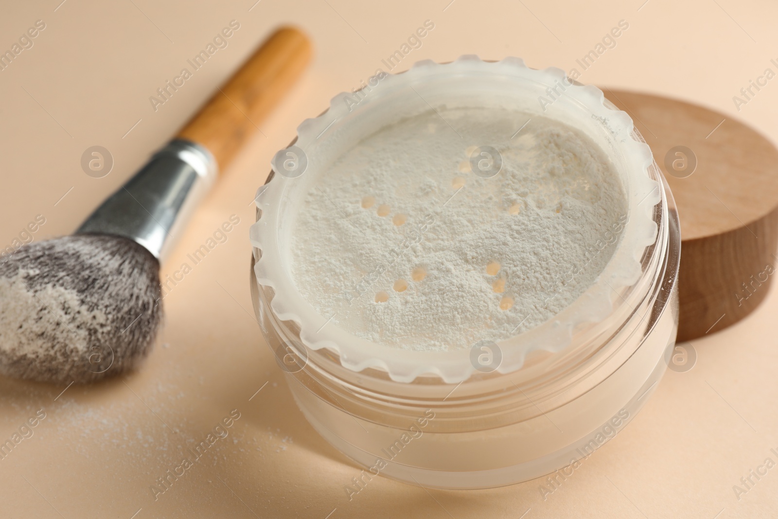 Photo of Rice loose face powder and makeup brush on beige background, closeup