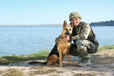 Man in military uniform with German shepherd dog near river, space for text