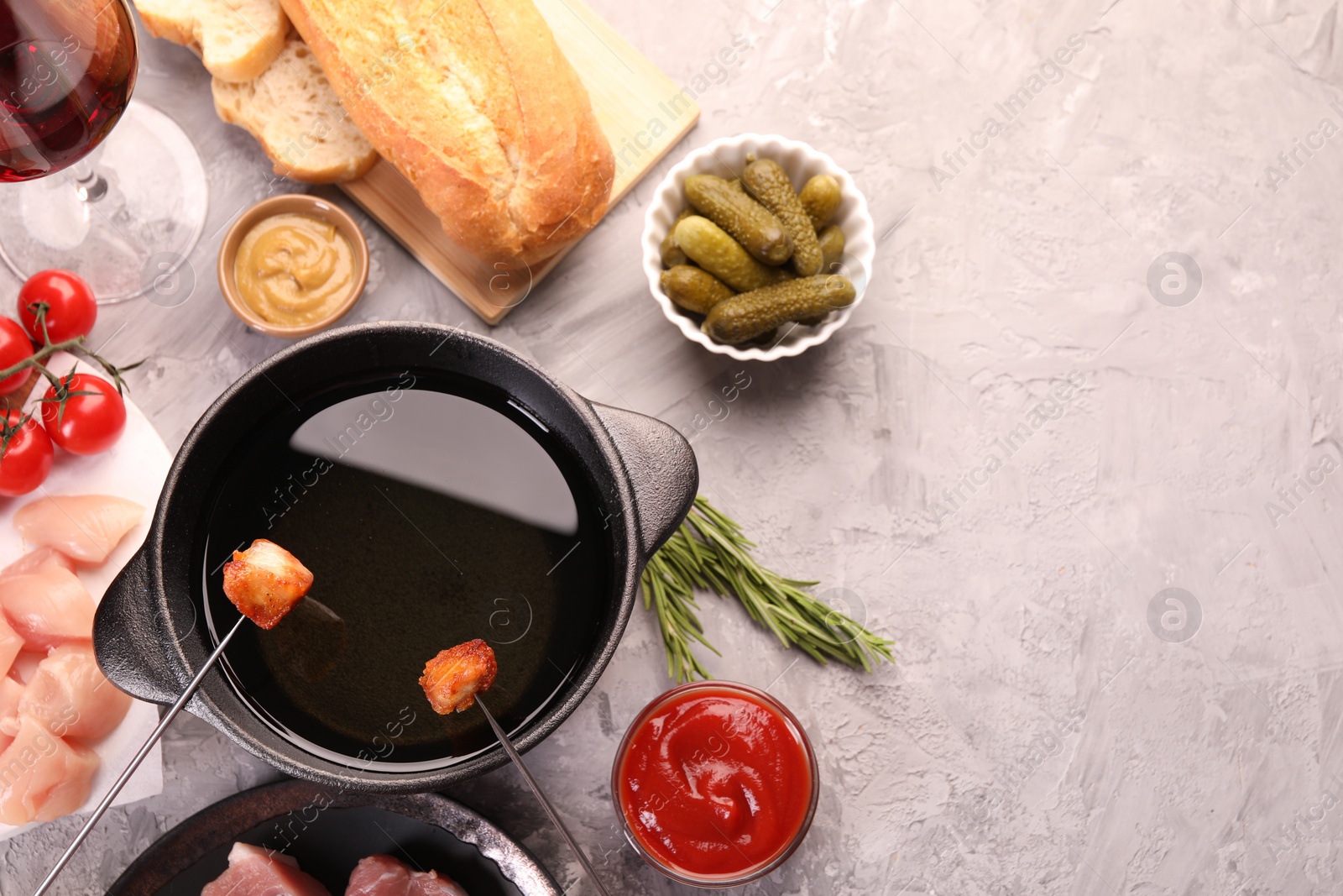 Photo of Fondue pot, forks with fried meat pieces, pickled cucumbers and other products on grey textured table, flat lay. Space for text