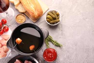 Fondue pot, forks with fried meat pieces, pickled cucumbers and other products on grey textured table, flat lay. Space for text