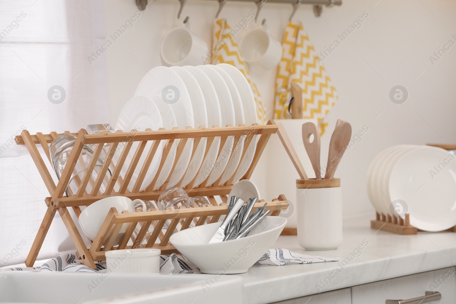 Photo of Drying rack with clean dishes and cutlery on countertop in kitchen