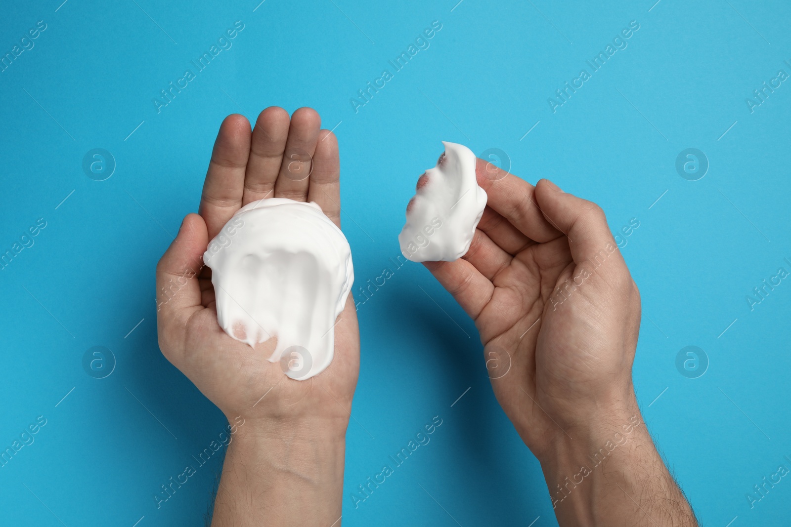 Photo of Man holding shaving foam on light blue background, top view