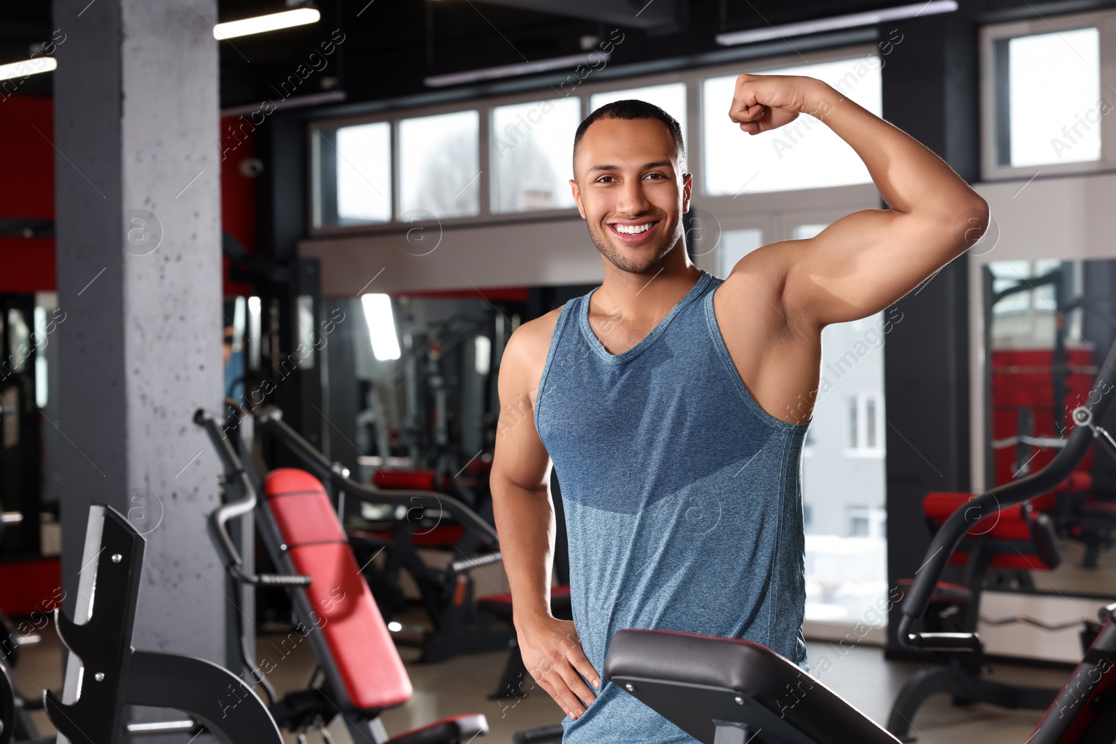 Photo of Happy trainer showing bicep in modern gym, space for text