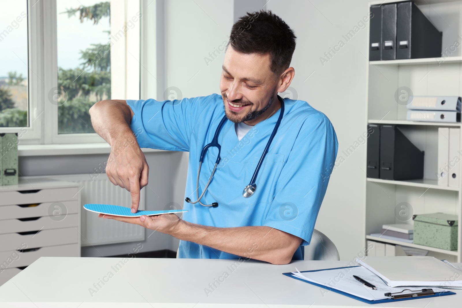 Photo of Handsome male orthopedist showing insole in hospital