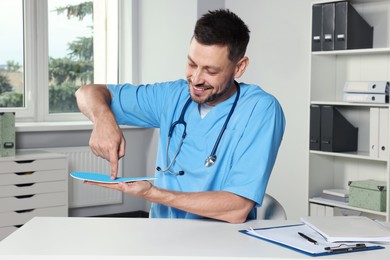 Handsome male orthopedist showing insole in hospital