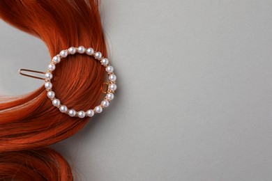 Elegant pearl clip and red hair strand on white background, top view. Space for text