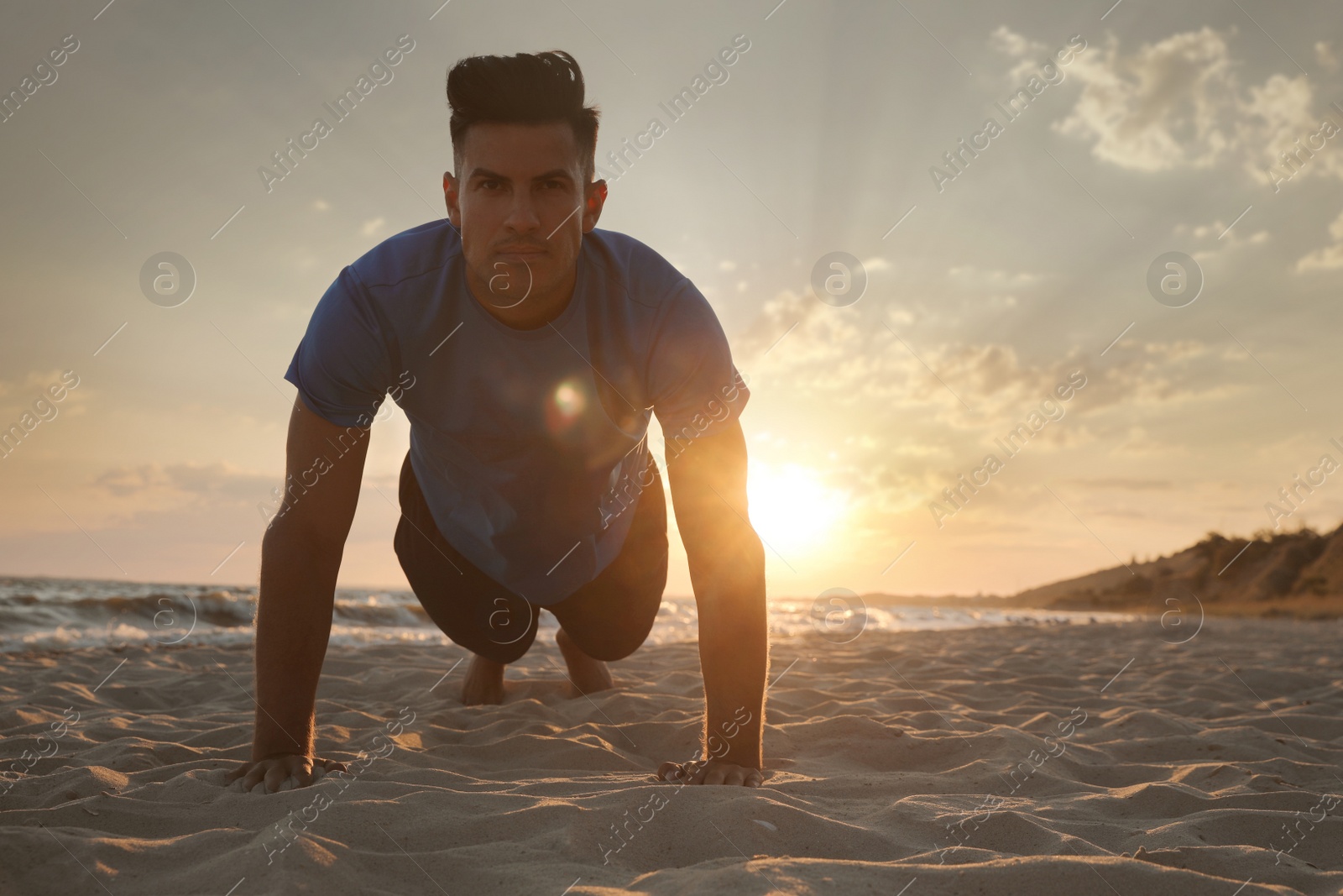 Photo of Sporty man doing plank on sandy beach at sunset