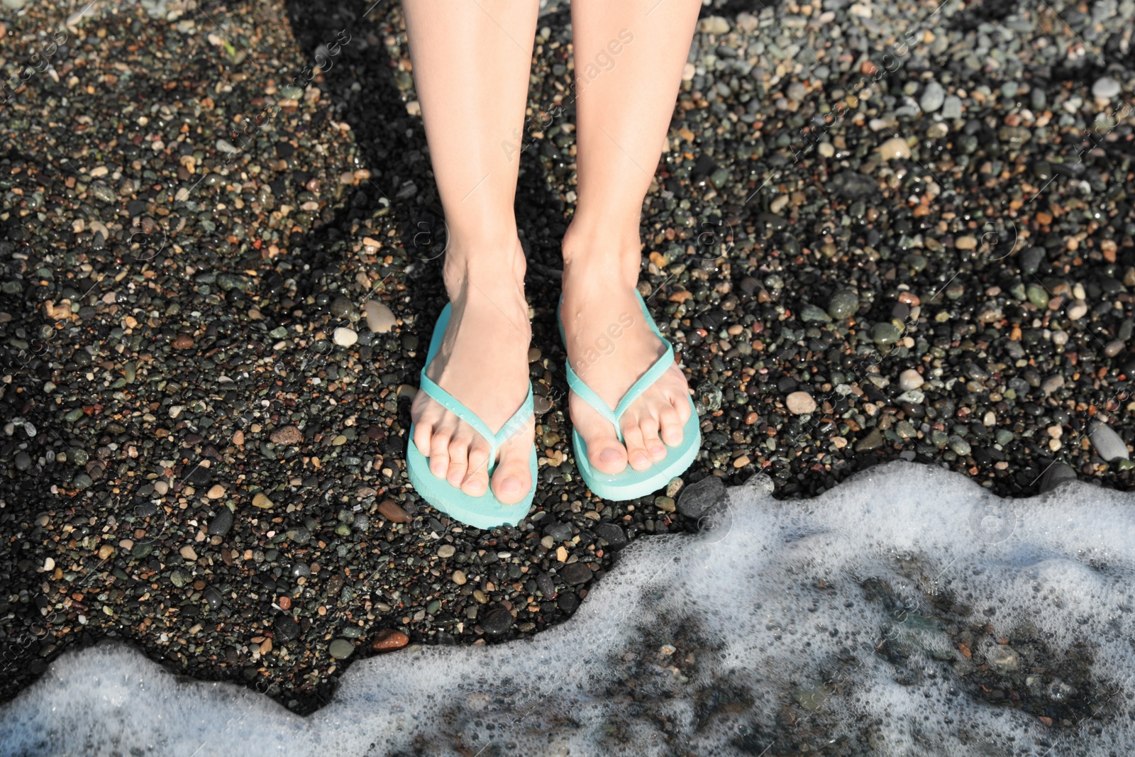 Photo of Woman in stylish flip flops on pebble beach near beautiful sea wave, closeup