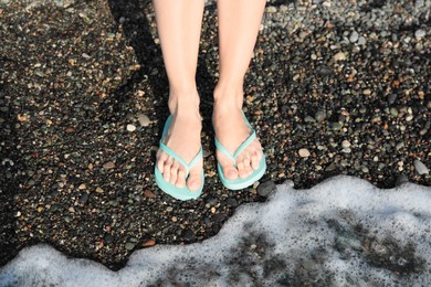 Photo of Woman in stylish flip flops on pebble beach near beautiful sea wave, closeup