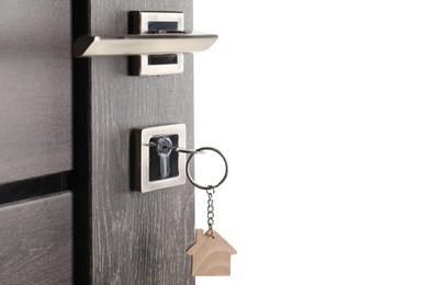 Photo of Mortgage and real estate. Open door with key and house shaped keychain on white background, space for text