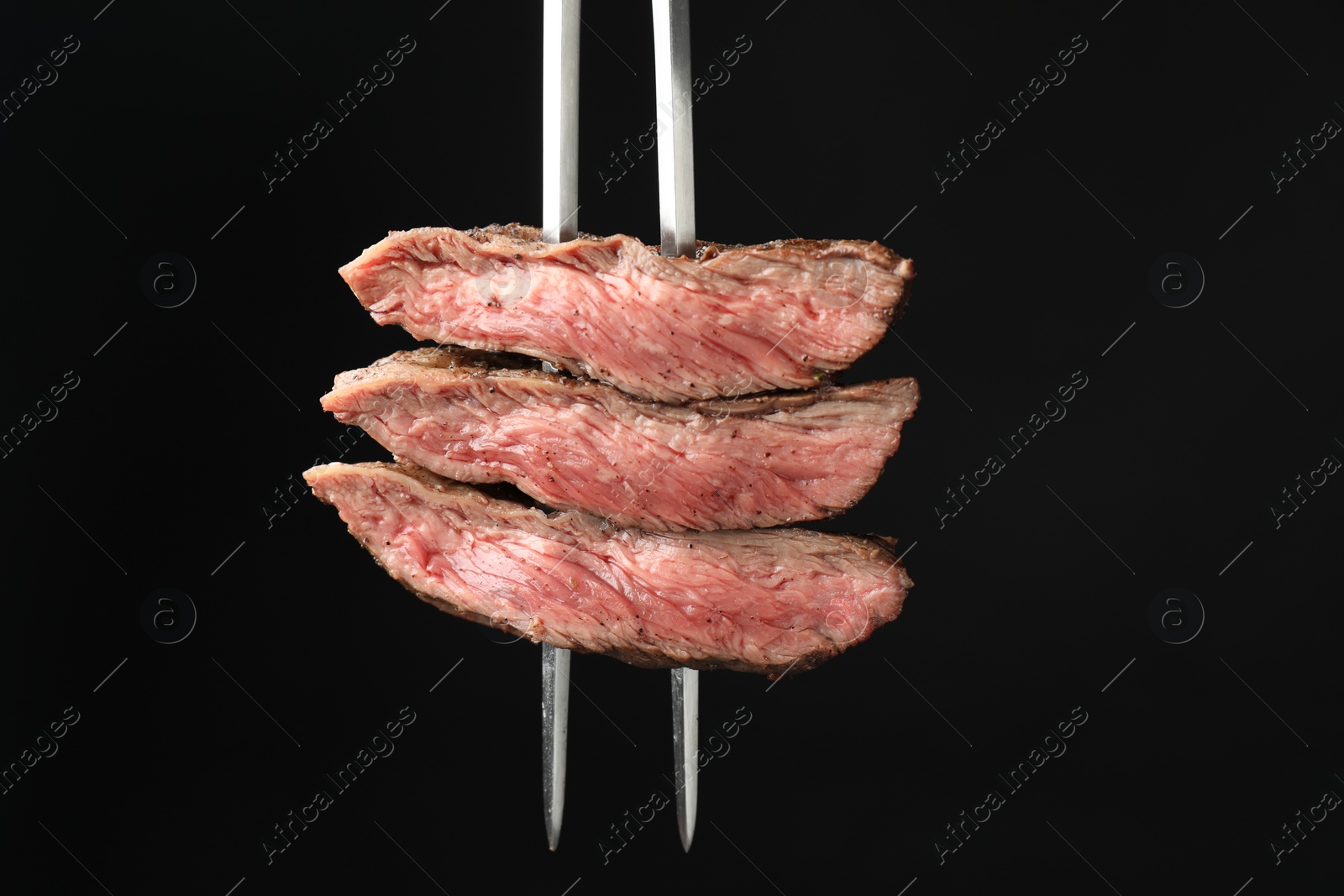 Photo of Meat fork with grilled beef pieces on black background, closeup