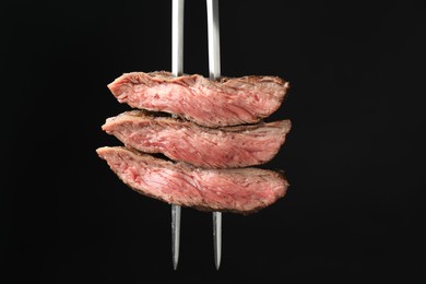 Photo of Meat fork with grilled beef pieces on black background, closeup