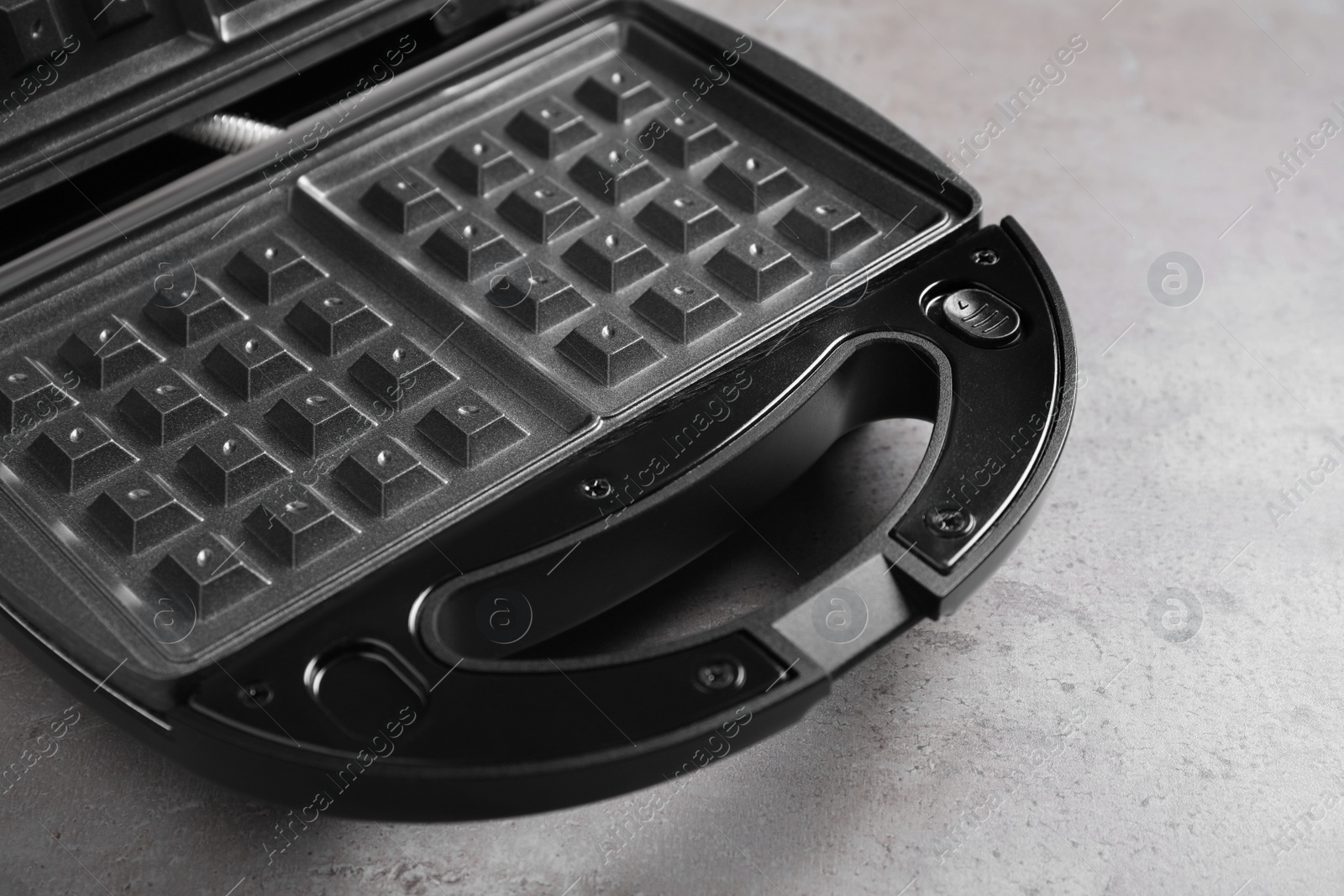 Photo of Modern waffle iron on grey stone table, closeup