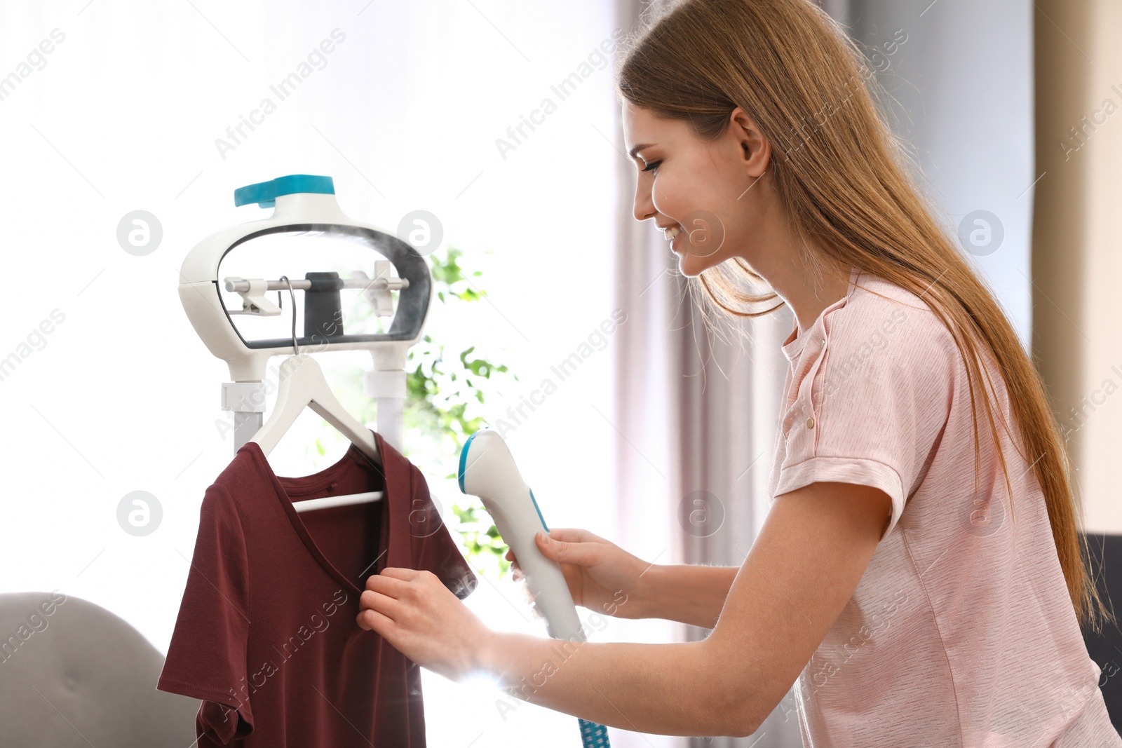 Photo of Young woman steaming her clothes on rack at home