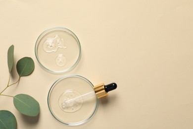 Photo of Petri dishes with samples of cosmetic oil, pipette and eucalyptus leaves on beige background, flat lay. Space for text