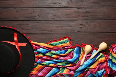 Photo of Mexican sombrero hat, maracas and colorful poncho on wooden background, flat lay. Space for text