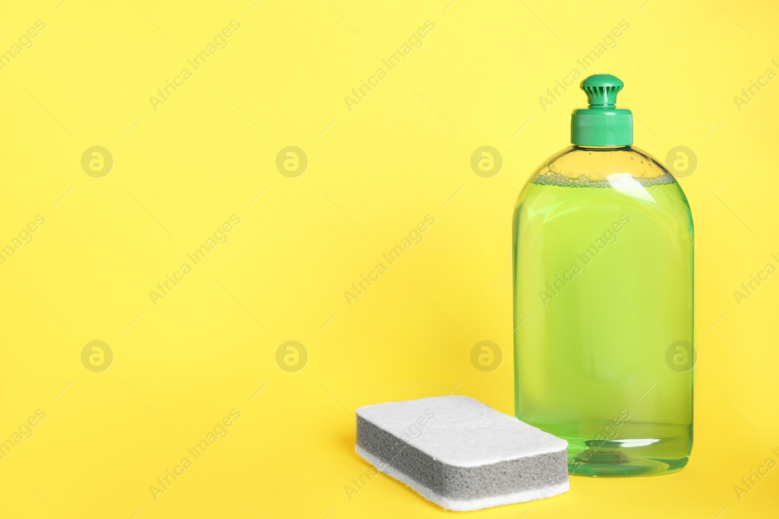 Photo of Detergent and sponge on yellow background, space for text