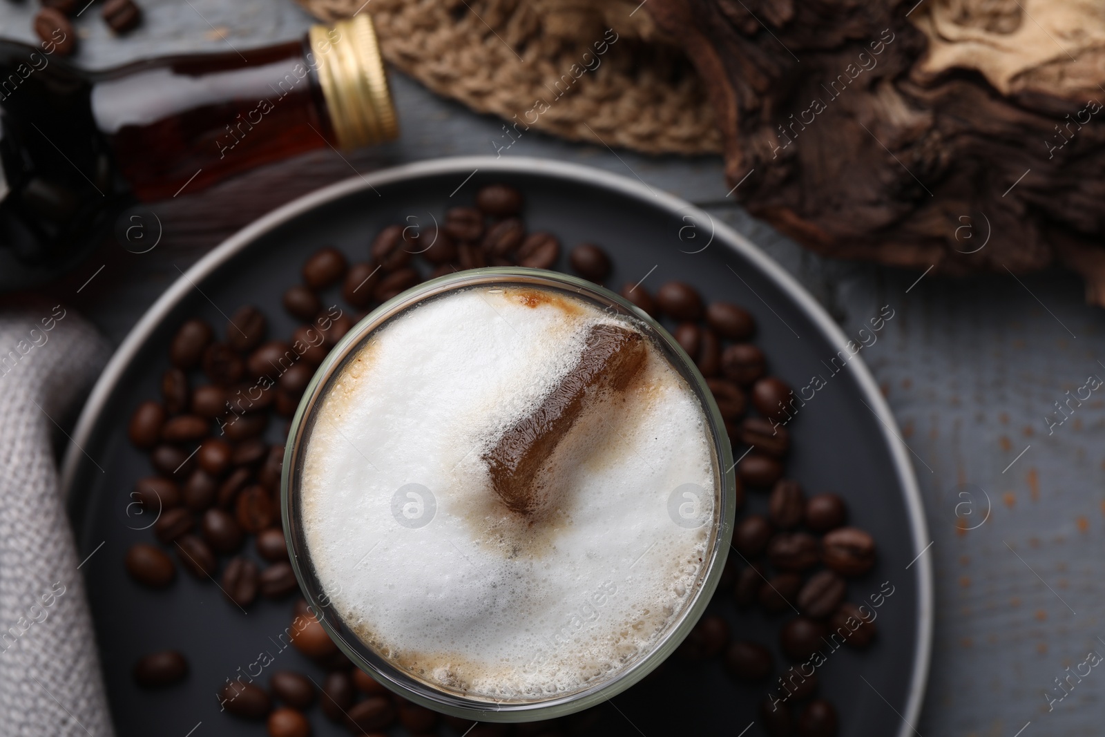 Photo of Glass of coffee, bottle with delicious syrup and beans on light grey table, closeup