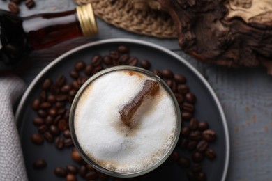 Photo of Glass of coffee, bottle with delicious syrup and beans on light grey table, closeup