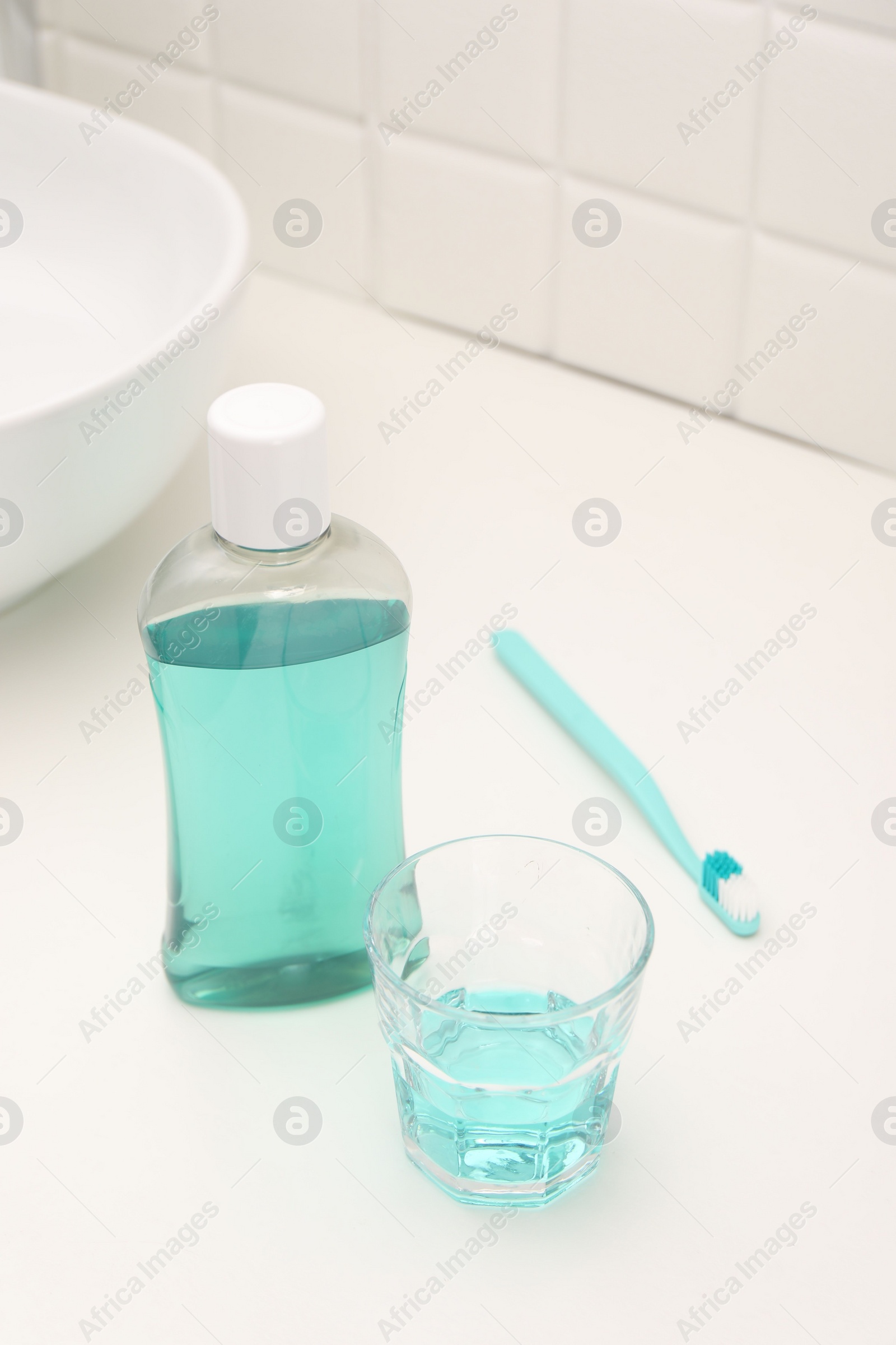 Photo of Bottle of mouthwash, toothbrush and glass on white table in bathroom