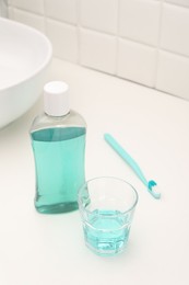 Bottle of mouthwash, toothbrush and glass on white table in bathroom