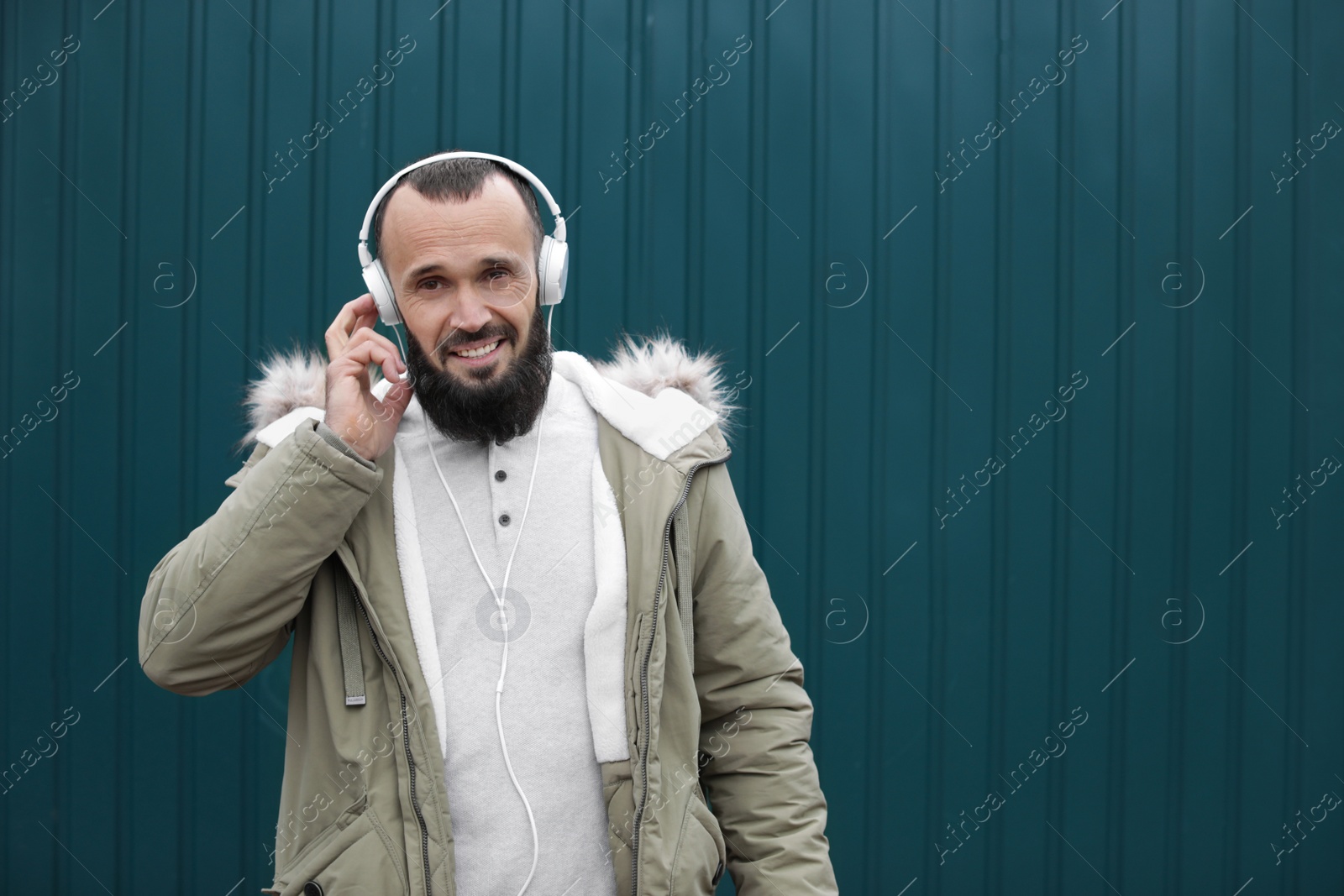 Photo of Mature man with headphones listening to music near color wall. Space for text