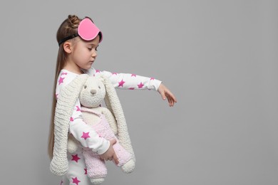 Photo of Girl in pajamas and sleep mask with toy bunny sleepwalking on gray background, space for text