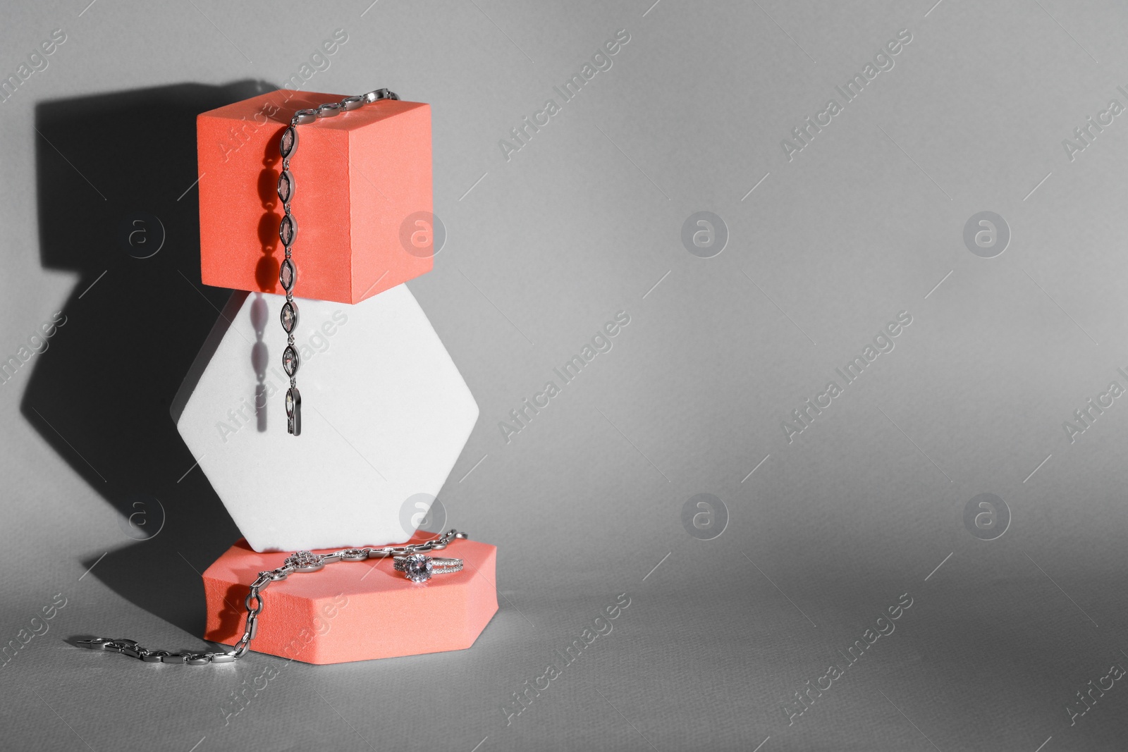 Photo of Elegant jewelry. Stylish presentation of luxury bracelets and ring on podiums against gray background. Space for text