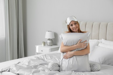 Beautiful woman hugging pillow on comfortable bed with silky linens, space for text