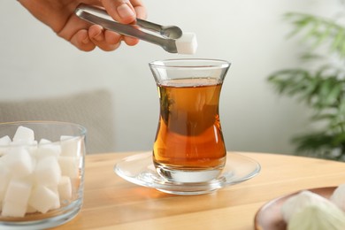 Photo of Woman adding sugar cube into aromatic tea at wooden table indoors, closeup