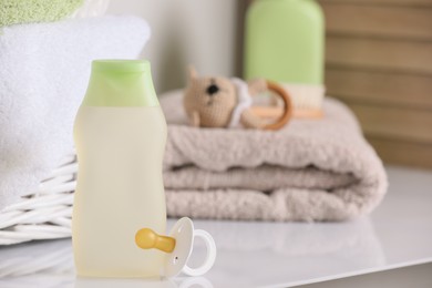 Bottle of baby cosmetic product and pacifier near accessories on white table. Space for text