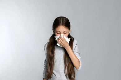 Photo of Little girl blowing nose into paper tissue on light grey background. Seasonal allergy