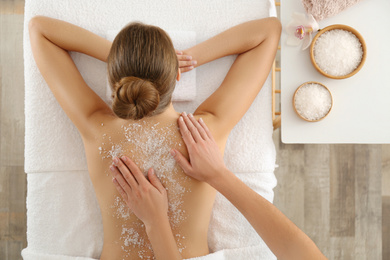 Photo of Young woman having body scrubbing procedure with sea salt in spa salon, top view