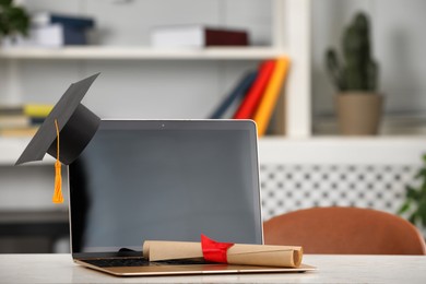 Photo of Graduation hat, student's diploma and laptop on white table indoors