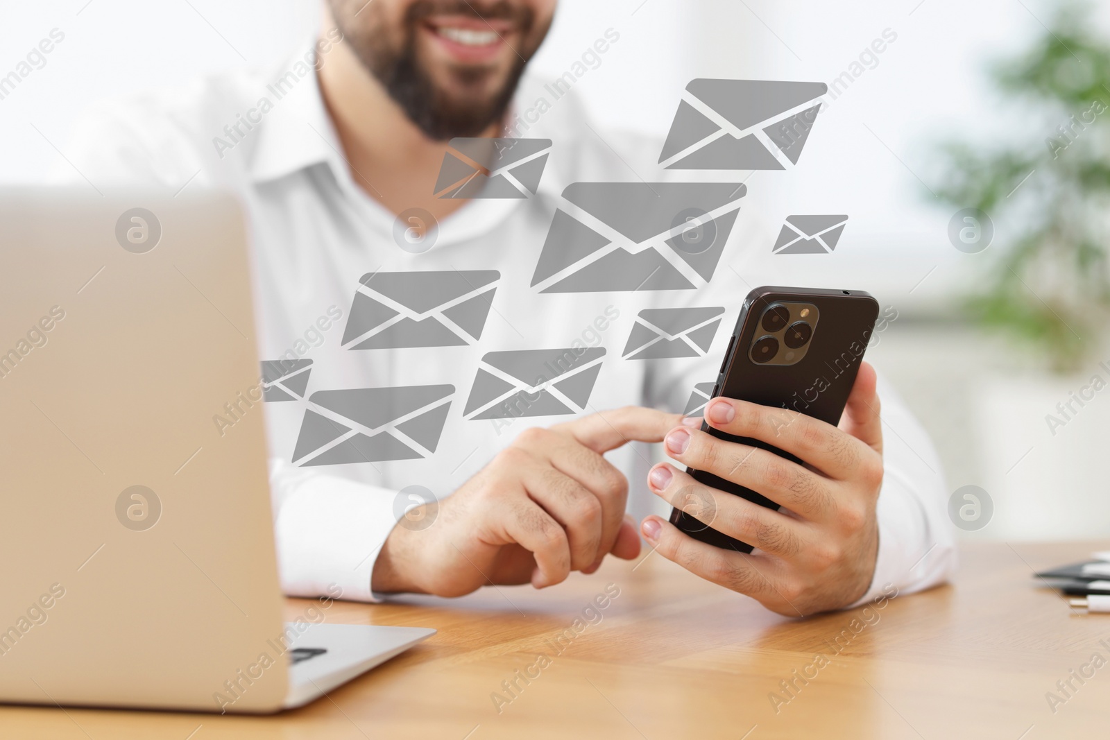 Image of Smiling man with smartphone chatting at table indoors, closeup. Many illustrations of envelope as incoming messages out of device