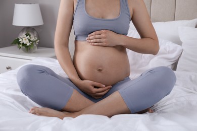 Photo of Pregnant woman sitting on bed at home, closeup