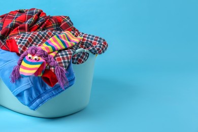 Photo of Laundry basket overfilled with child clothes on light blue background. Space for text