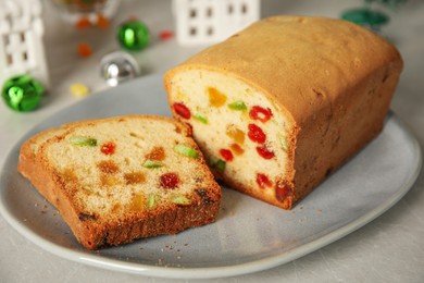 Delicious cake with candied fruits and Christmas decor on light grey table, closeup