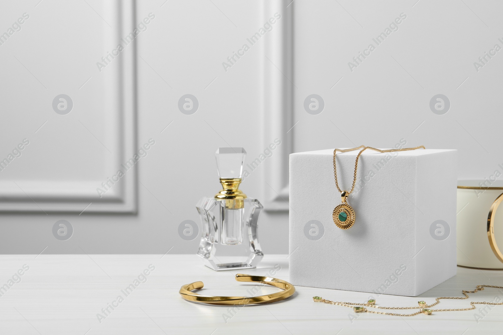 Photo of Stylish presentation of bijouterie on podium and perfume bottle on white wooden table, space for text