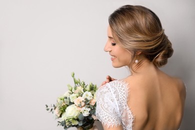 Photo of Young bride with elegant hairstyle holding wedding bouquet on beige background